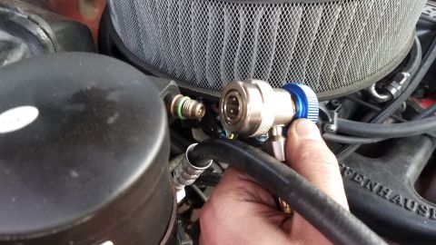 1985 Ford Bronco - Close-up of a hand connecting an air conditioning hose fitting to a vehicle's AC system.