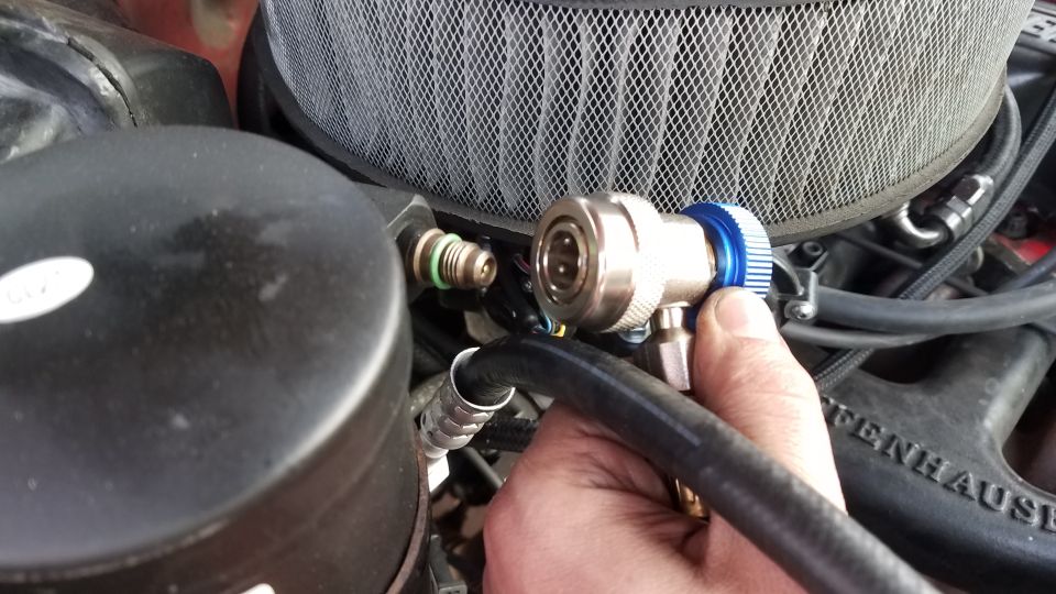 Hand connecting AC hose fitting to vehicle component, with air filter visible