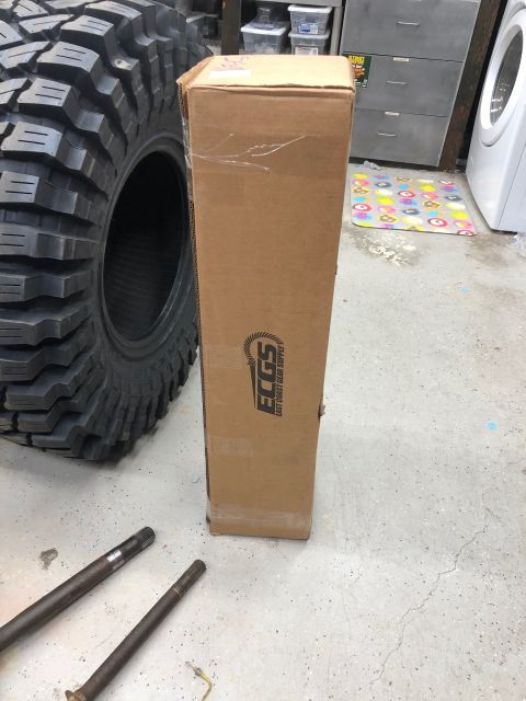 1992 Jeep Wrangler - A cardboard box from East Coast Gear Supply sits beside a large off-road tire and axle shafts.