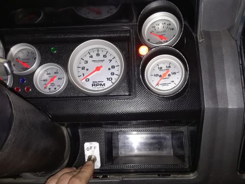 1985 Ford Bronco - A collection of aftermarket gauges are visible on a vehicle's dashboard, with a hand operating a toggle switch.