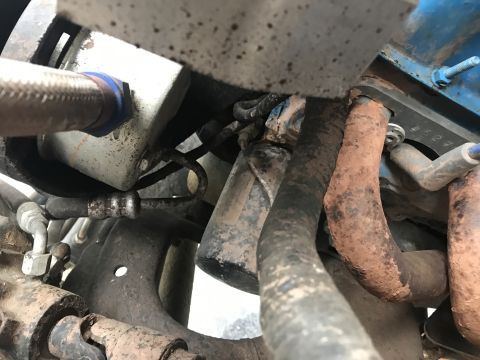 1989 Ford Bronco - Close-up view of engine components including hoses and a rusty exhaust manifold.