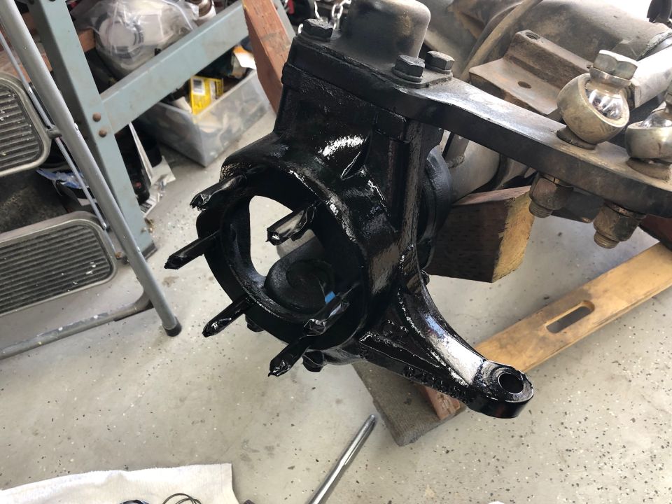 Painted front axle knuckle assembly with studs protruding from the hub area. A metal bracket with bolts is attached to the top