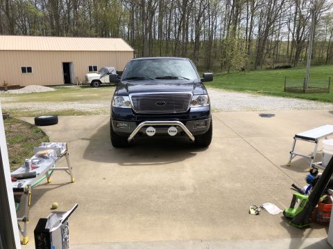 2005 Ford F-150 - A dark blue pickup truck is parked in a driveway with a garage and trees in the background. A second white truck is parked near the garage.