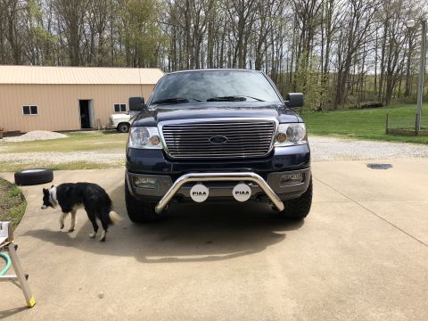 2005 Ford F-150 - Dark blue Ford F-150 truck with a chrome bull bar and PIAA lights is parked outside a building.