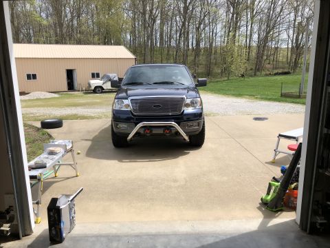 2005 Ford F-150 - A dark blue 2005 Ford F-150 pickup truck is parked in a garage, facing forward with a chrome grille guard.