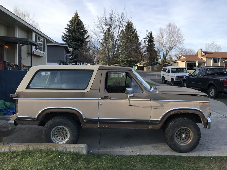 Two-tone brown Ford Bronco parked on a residential street, with a white SUV and black pickup truck behind it