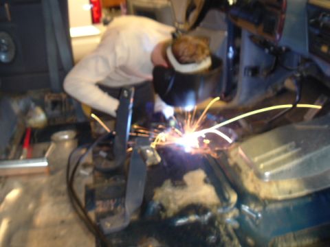 1989 Ford Bronco - A person in a welding mask works on the floor pan of a vehicle, with bright sparks illuminating the scene.