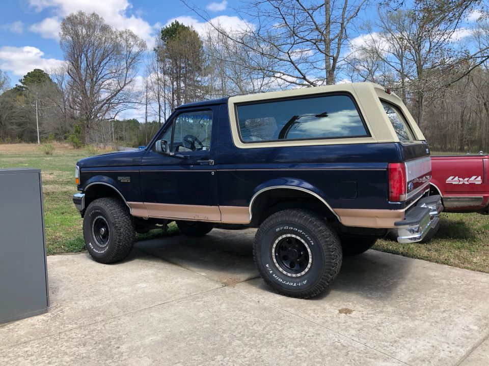 Side view of a 1995 Ford Bronco, dark blue with tan trim and a removable top