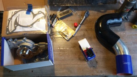 New water pump, gasket set, and intake pipe with tools on a workbench
