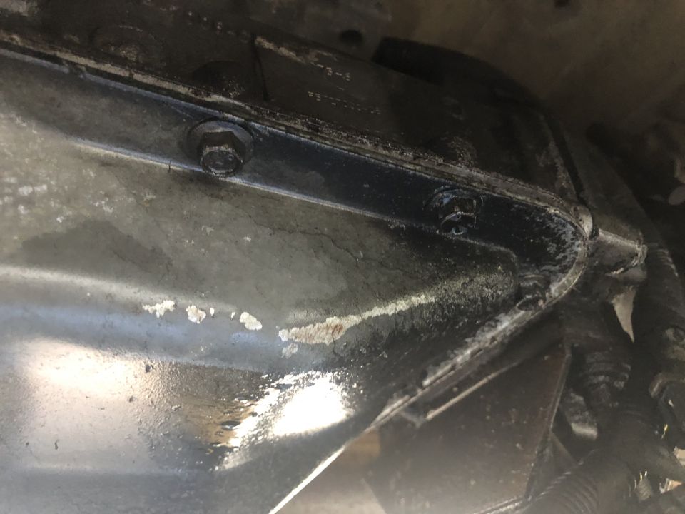 Underside view of a vehicle's transmission pan with bolts visible