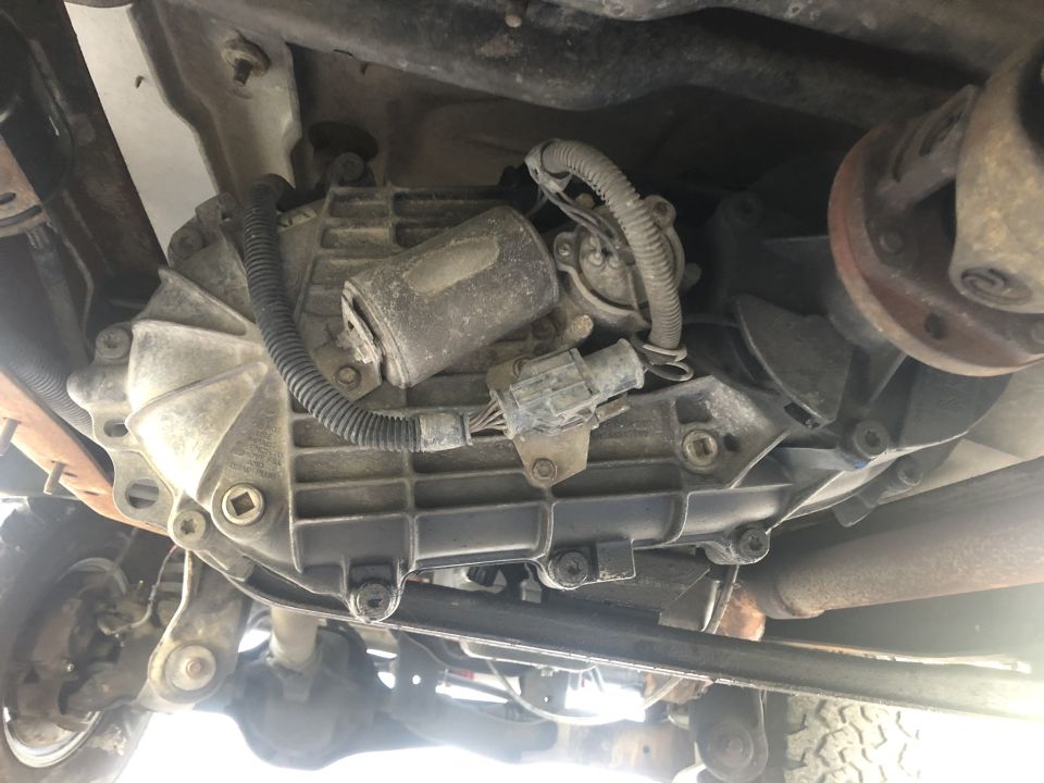 Underside view of a vehicle's transmission and transfer case with wiring and driveshaft connections visible