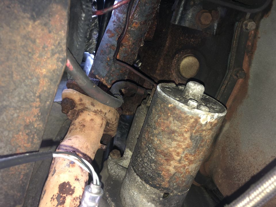 Rusty starter motor and exhaust manifold with visible wiring and hose.