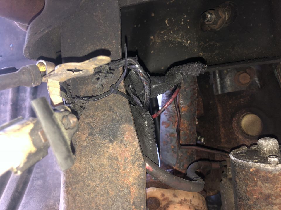 Damaged wiring harness and rusted metal parts under a vehicle.