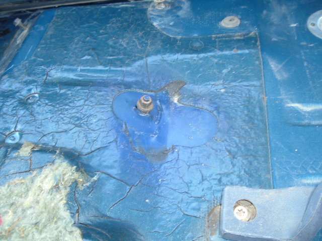 Cracked blue interior floor pan with a bolt stud and body mount bracket