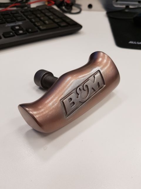 1978 Ford Bronco - A close-up shot shows a bronze-colored shift knob with the B&M logo embossed on it, attached to a threaded bolt. The shift knob is resting…