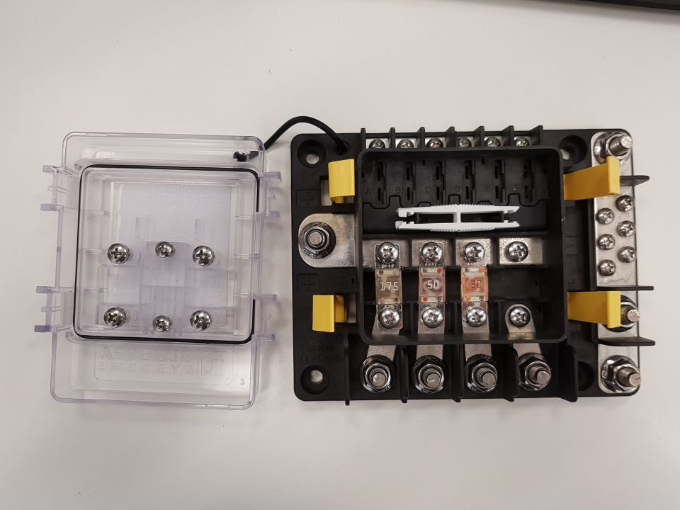 Fuse box with clear cover open, showing fuses and terminals.