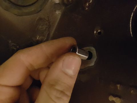 1978 Ford Bronco - A hand is holding a small metal cylindrical part near a hole in a dark-colored surface, possibly a vehicle panel.