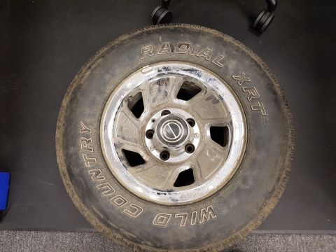 1978 Ford Bronco - A close-up, top-down view of a single tire and chrome rim, likely for a 1978 Ford Bronco. The tire has raised white lettering that reads "W…