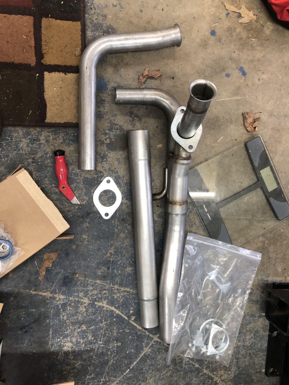 New unpainted exhaust pipes, gasket, and clamp hardware laid out on a concrete garage floor.