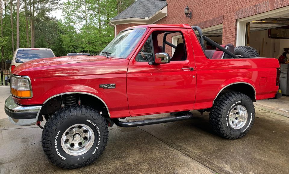 Red Ford Bronco with aftermarket wheels and tires parked on a wet driveway.