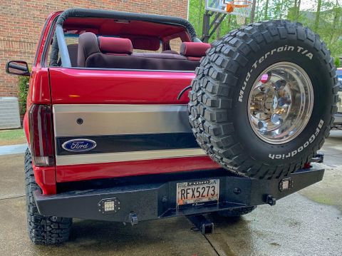 1994 Ford Bronco - The rear view of a red Ford Bronco with a spare tire mounted on the back. The vehicle has a custom black bumper with LED lights and a licen…