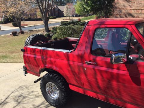 1994 Ford Bronco - The right side of a bright red Ford Bronco is shown parked on a concrete driveway. A spare tire is mounted in the bed of the truck.