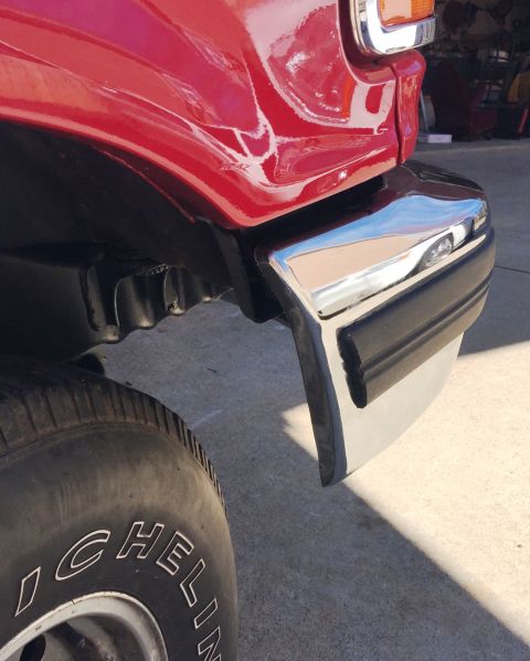 1994 Ford Bronco - A close-up view of the front fender and chrome bumper of a red vehicle, with a portion of a tire visible in the foreground. The vehicle app…