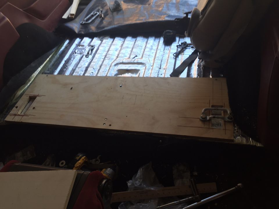 Wooden panel being installed on vehicle floor with hardware and tools.