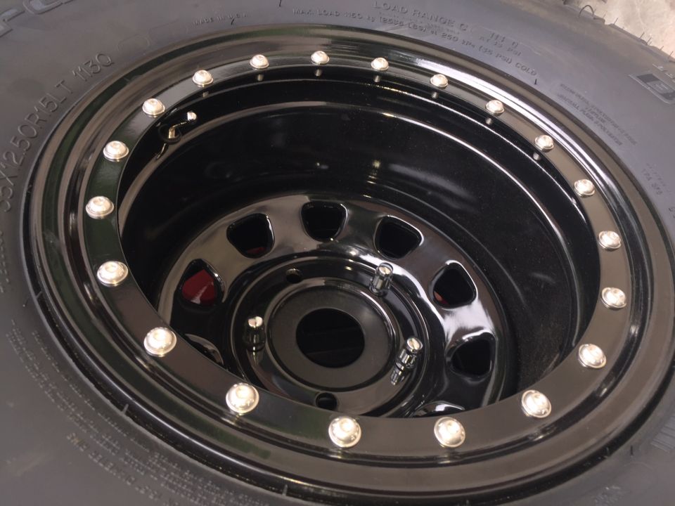 Close-up of a black aftermarket wheel with chrome lug nuts on a tire.
