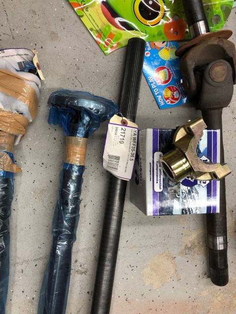 1992 Jeep Wrangler - Several automotive axle shafts and a universal joint are laid out on a concrete floor. One axle shaft has a yellow and purple tag with part…