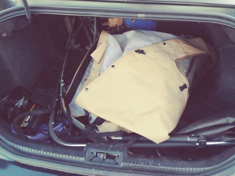 1996 Ford Bronco - The open trunk of a vehicle contains a folded stroller or similar item, a helmet, and a black bag with a yellow and black label. A tan fabr…