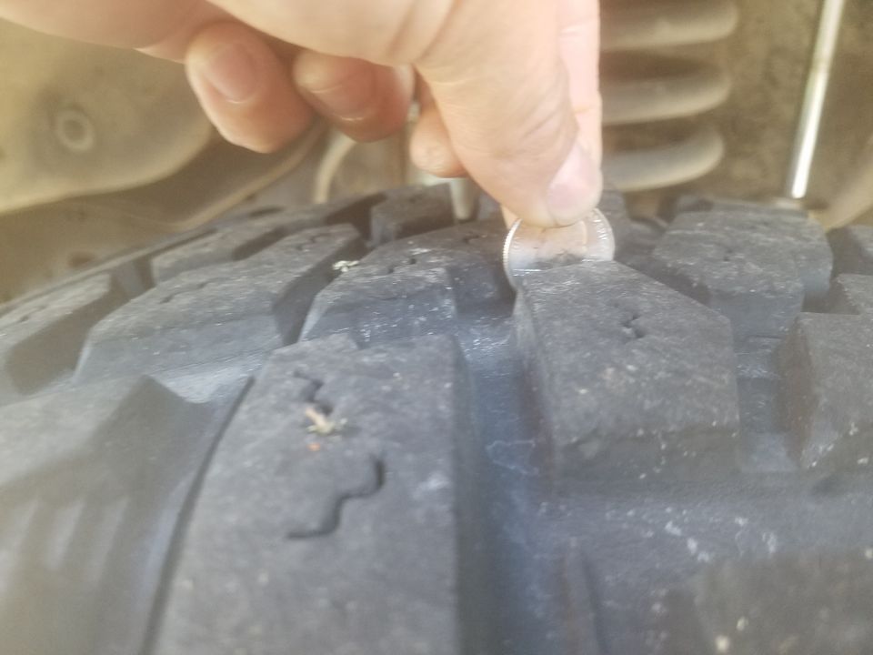 Hand holding a quarter to measure tread depth on a large off-road tire.