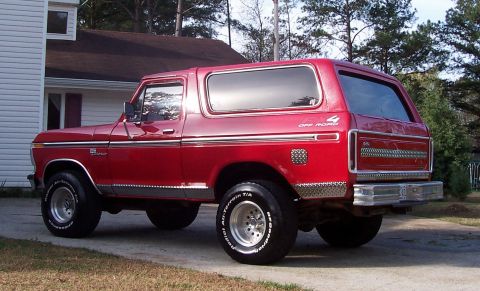 1979 Ford Bronco - This red Ford Bronco is parked in front of a house with trees in the background.