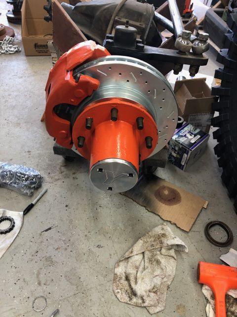 1992 Jeep Wrangler - A close-up view of a vehicle's brake caliper and rotor assembly, painted bright orange, is shown on a concrete floor next to various tools…