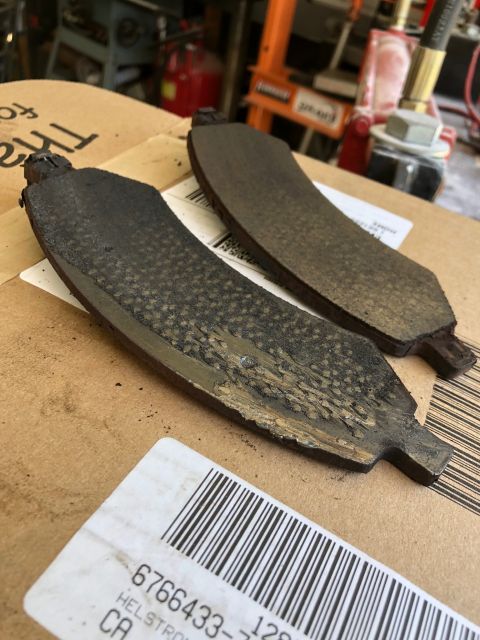 1992 Jeep Wrangler - Two worn-out brake pads are shown resting on a cardboard box. The pads exhibit significant wear, with the friction material heavily degrade…