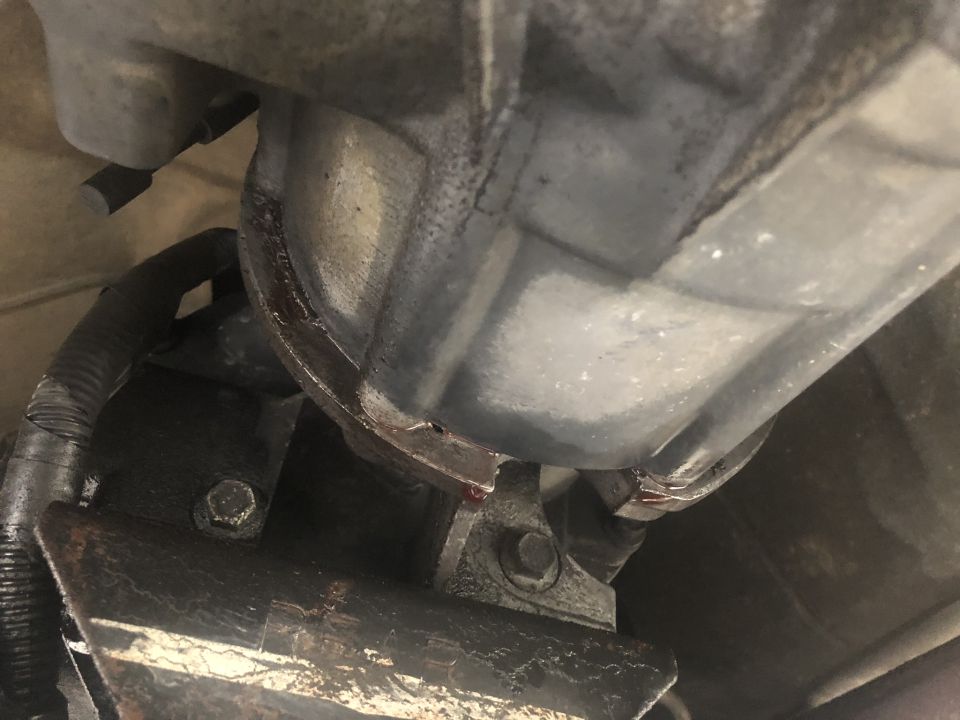 Vehicle transmission leak, red fluid dripping from housing onto bracket.