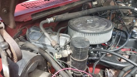 1985 Ford Bronco - A close-up view of the engine bay of a red vehicle, showing the air filter housing, various hoses, and engine components.