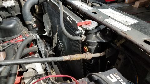 1985 Ford Bronco - Close-up view of the engine bay of a 1985 Ford Bronco, focusing on the radiator and hoses. The radiator has a red cap and is connected to t…