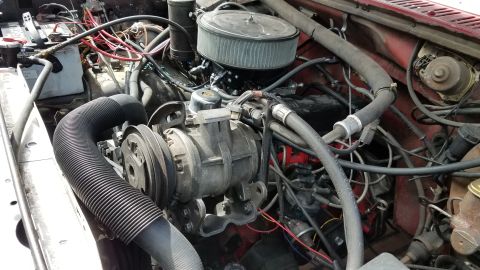1985 Ford Bronco - The engine bay of a red Ford Bronco shows a complex arrangement of hoses, wires, and engine components including the air filter housing, al…