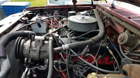 1985 Ford Bronco - The engine bay of a red Ford Bronco is shown, featuring a V8 engine with an aftermarket air filter and various hoses and wiring. The vehicl…