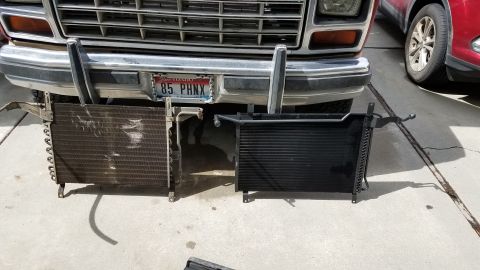 1985 Ford Bronco - A close-up, low-angle view of the front of a vintage Ford Bronco, with two car radiators laid out on the concrete driveway in front of it.…