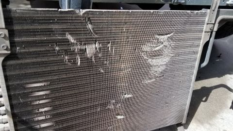 1985 Ford Bronco - The image shows a damaged condenser or radiator unit with bent and torn fins. The metal fins are coated in dust and debris, indicating it i…
