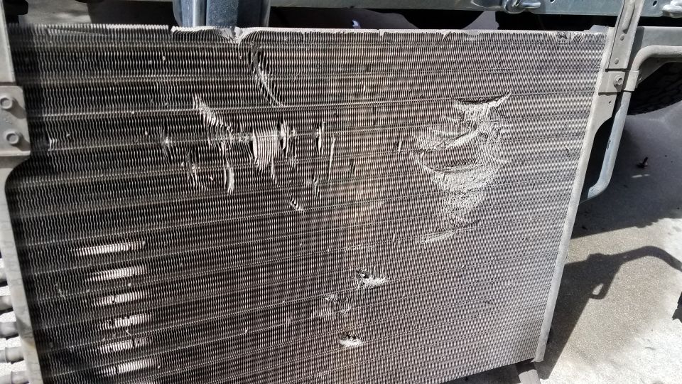 Damaged vehicle radiator or condenser unit with bent and torn fins.