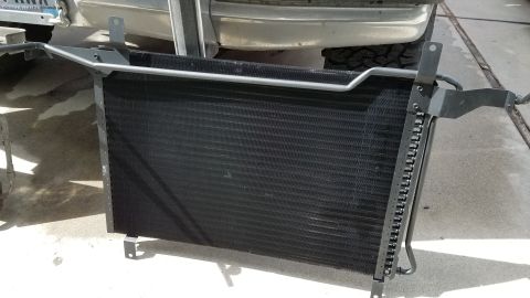 1985 Ford Bronco - A black car radiator or condenser is shown mounted on metal brackets. The part is positioned outdoors on a concrete surface, with the rear…
