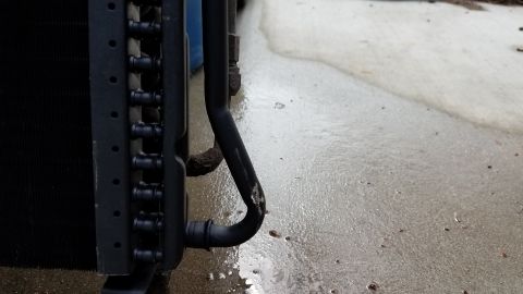1985 Ford Bronco - A close-up view of an air conditioning compressor, likely from a vehicle, with a black hose connected.