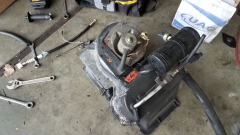 1985 Ford Bronco - Disassembled air conditioning unit with hoses and fan, lying on a garage floor with tools.