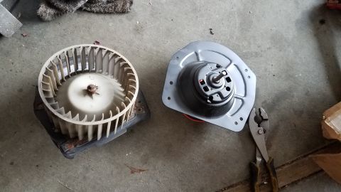 1985 Ford Bronco - Two parts of a vehicle's HVAC system, a blower motor and its fan, are laid out on a concrete surface.