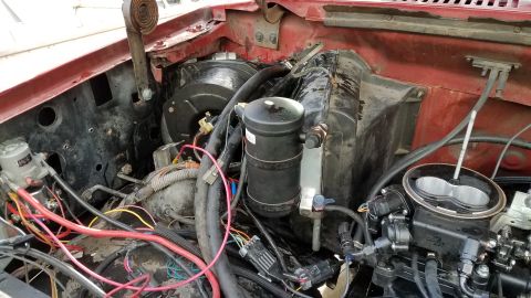 1985 Ford Bronco - The engine bay of a red Ford Bronco shows a complex setup of wiring, hoses, and engine components, including a black cylindrical accumulato…