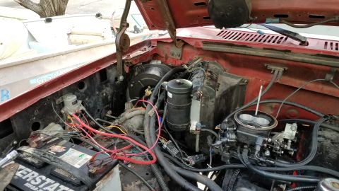 1985 Ford Bronco - The engine bay of a vehicle shows the carburetor, battery, and various hoses and wires.