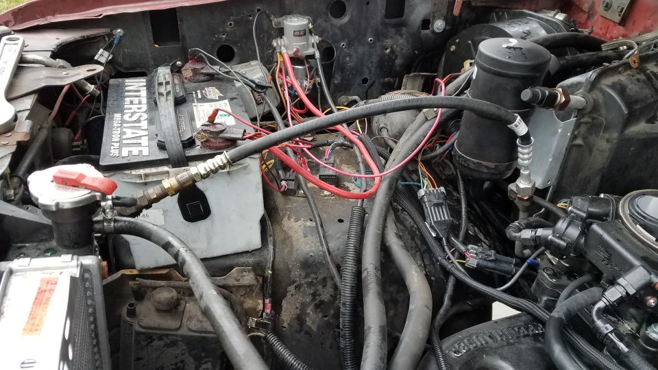 Engine bay with Interstate battery, hoses, wiring, and AC accumulator.